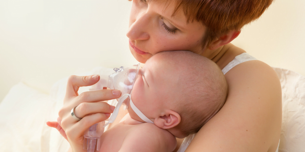 A mother holding and comforting her baby while administering breathing treatment with a nebulizer.