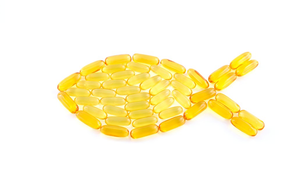 Fish shape creatively arranged using yellow omega-3 capsules on a white background, symbolizing fish oil supplements and heart health.