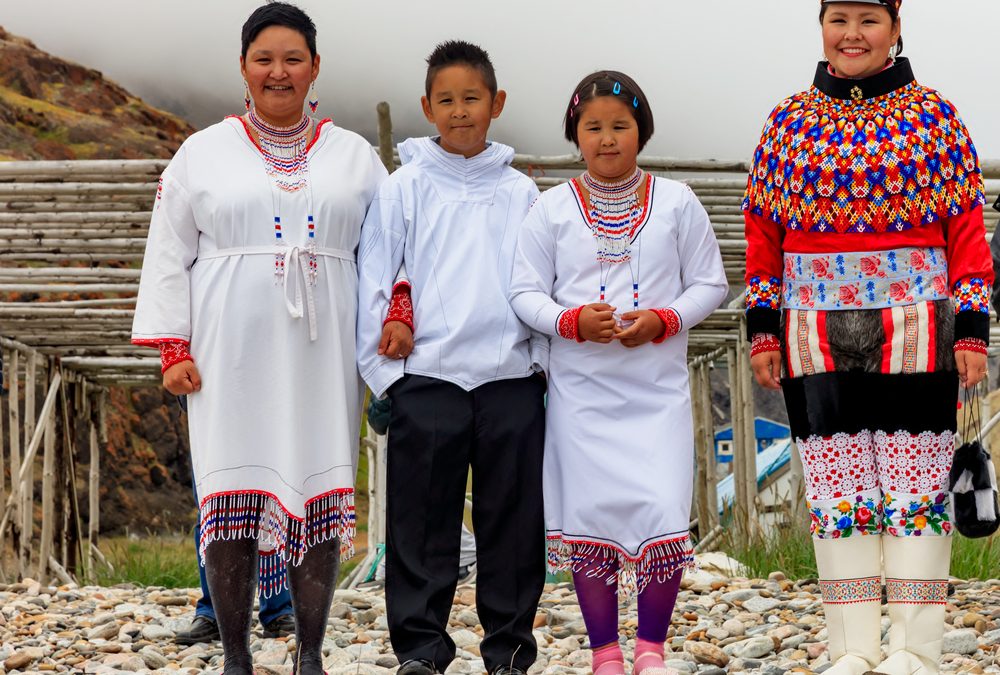 A group of Inuit or Greenlandic people, two women and two children, wearing traditional ceremonial clothing and elaborate beaded collars.