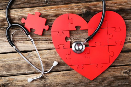 A red heart shape made of jigsaw puzzle pieces is lying on a rustic wooden surface.