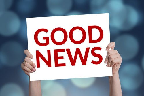Two hands hold up a white sign with the words GOOD NEWS written in large, bold red capital letters.