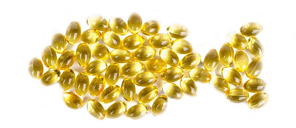 Yellow softgel capsules (fish oil) arranged in the shape of a fish on a white background.