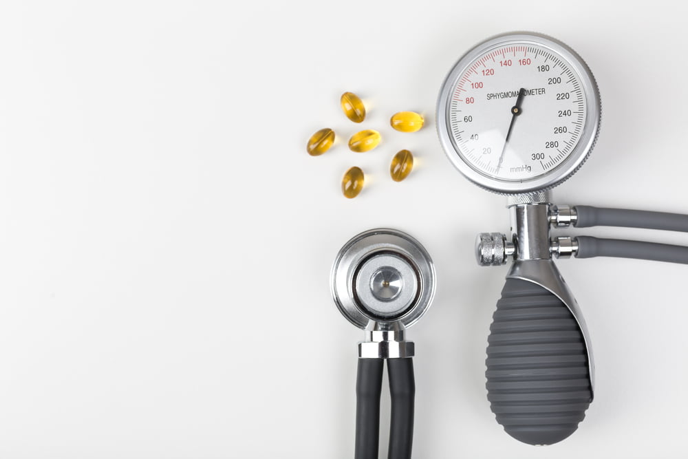 Medical devices (stethoscope and blood pressure cuff) with several yellow gel capsules on a white surface.