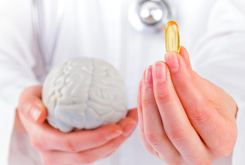 A doctor holding a large omega-3 fish oil capsule in one hand and a model of a human brain in the other, symbolizing the connection between omega-3 and brain health.
