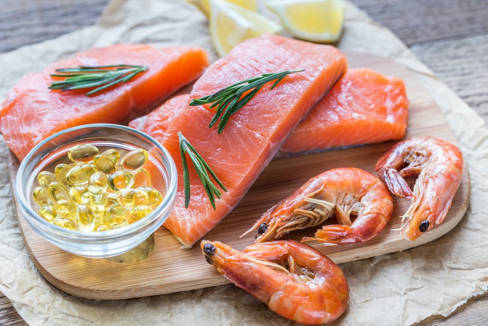 Raw salmon fillets, shrimp, and a bowl of **Omega-3 fish oil capsules** on a cutting board, representing sources of healthy fats.