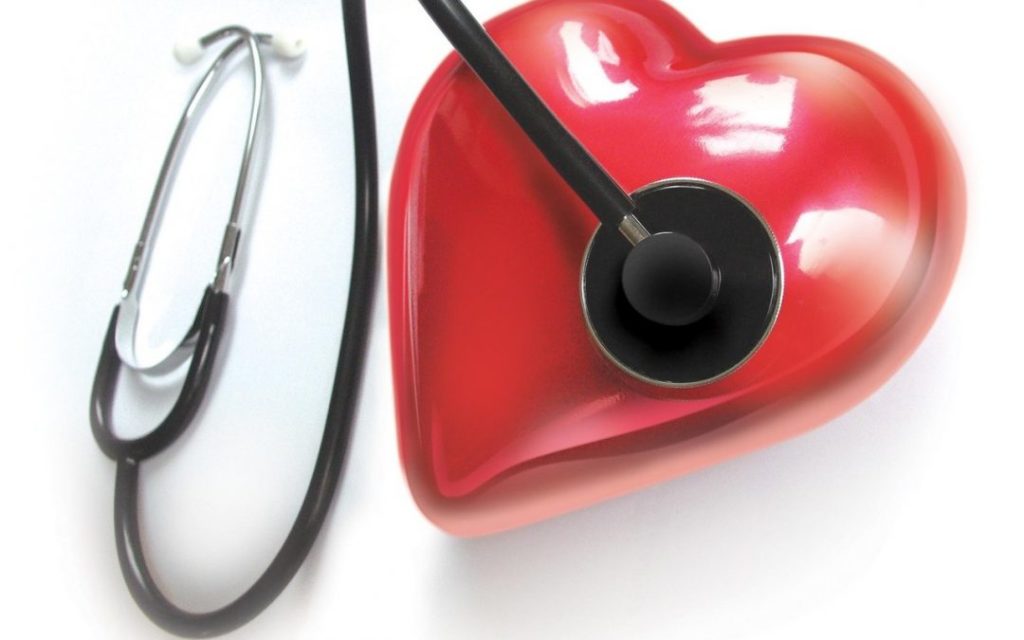 A stethoscope is placed on a large, three-dimensional, shiny red heart model with the background being solid white.