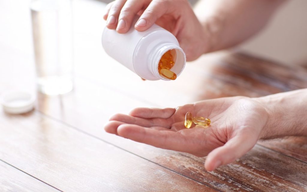 A person pouring yellow gel capsules (pills) from a white bottle into their hand.