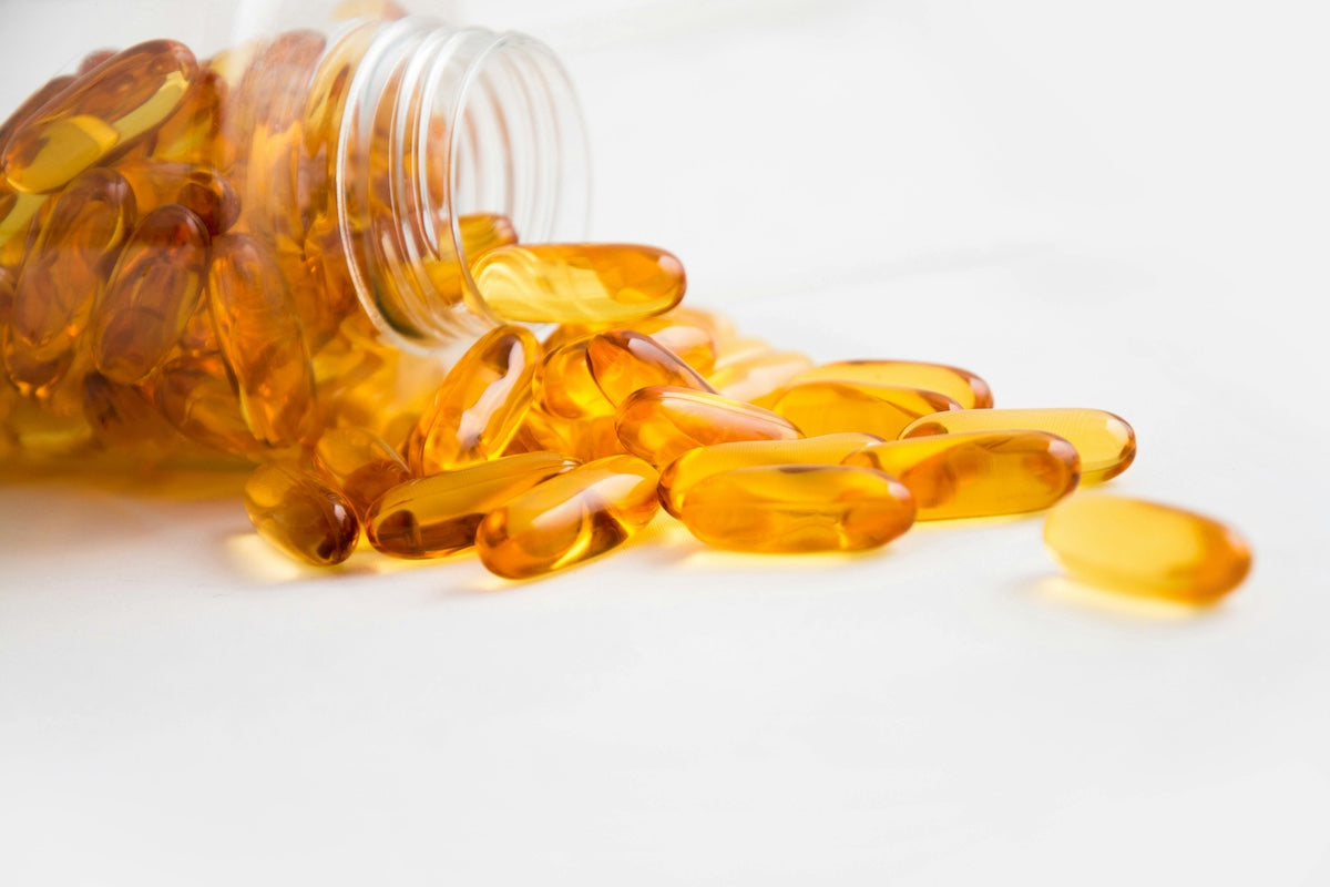 Golden yellow softgel capsules (pills) spilling out of an overturned clear plastic bottle onto a white surface.