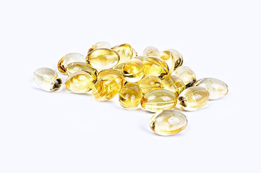 A close-up of a small pile of golden yellow softgel capsules on a bright white surface.