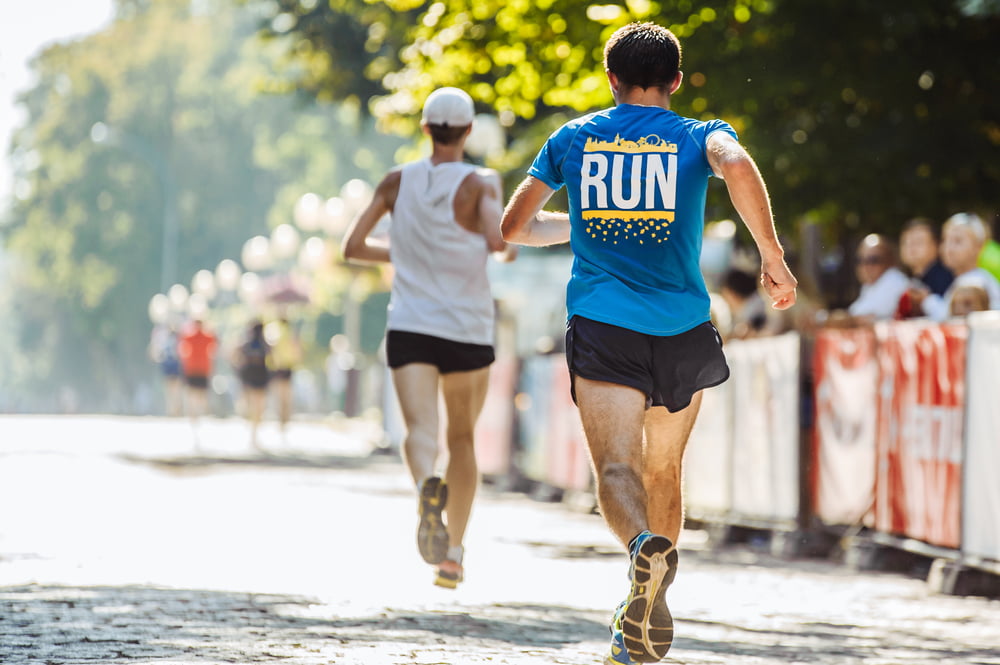 Runners competing in a marathon or road race, viewed from behind, with one wearing a blue shirt that says "RUN."