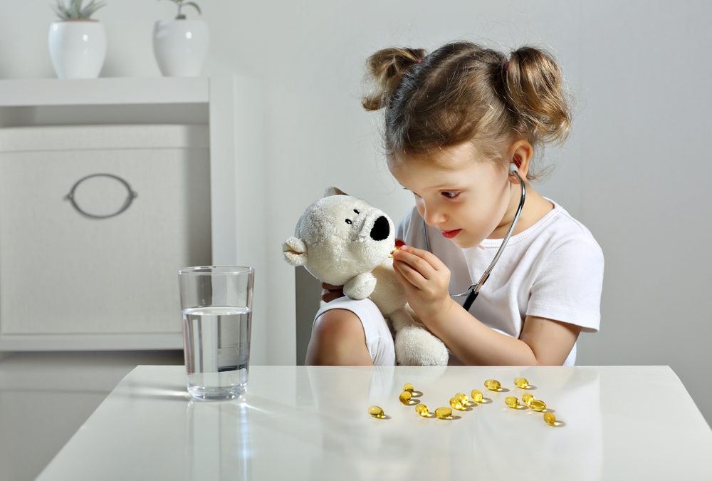 An adorable little girl with blonde hair in pigtails is playing doctor at a white table.