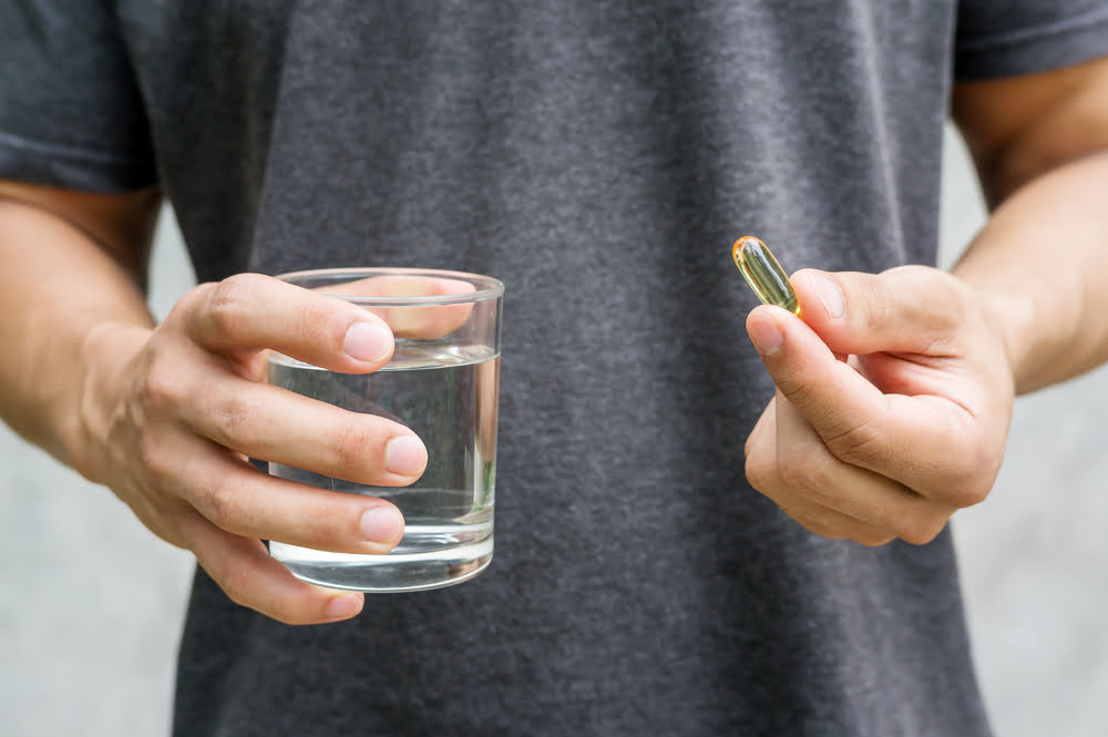 Man holding a glass of water and a capsule.