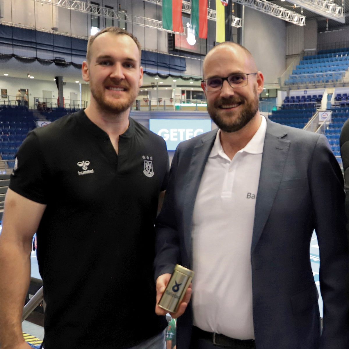 Two men standing together, one holding an award, in a sports arena setting.