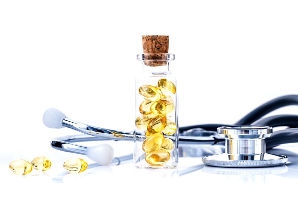 Glass jar filled with yellow omega-3 fish oil capsules, placed alongside a stethoscope on a white background, symbolizing health and medical care.