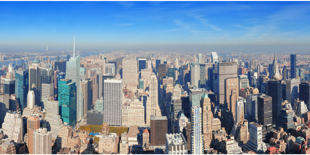 A panoramic, high-angle view of the Manhattan skyline in New York City on a clear day, dominated by dozens of closely packed skyscrapers.