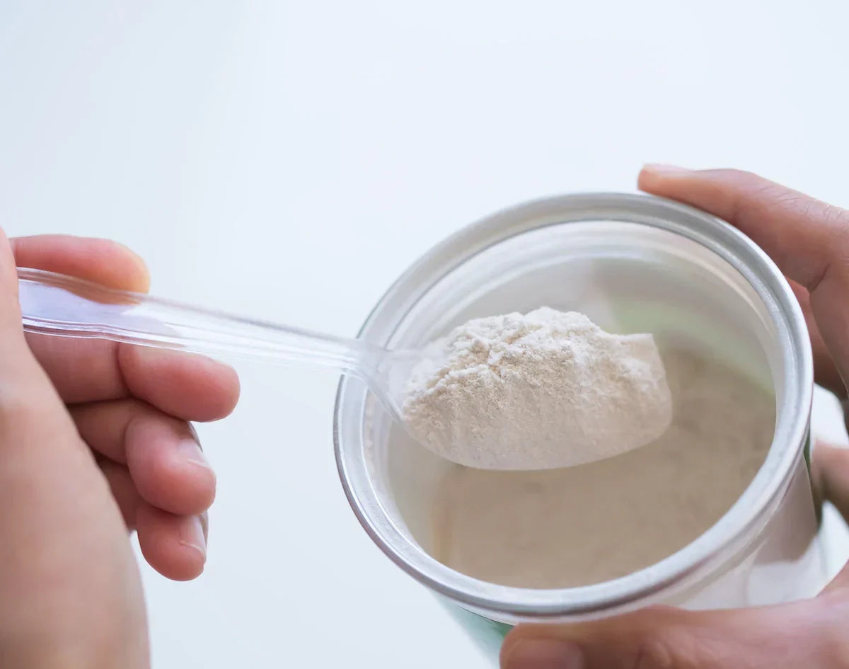 Person scooping collagen powder from a container with a spoon.