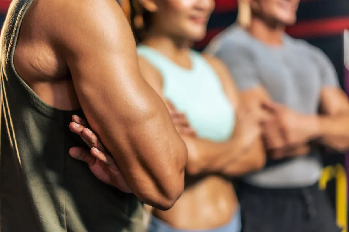 Person with a muscular arm in the foreground with two people in the background.