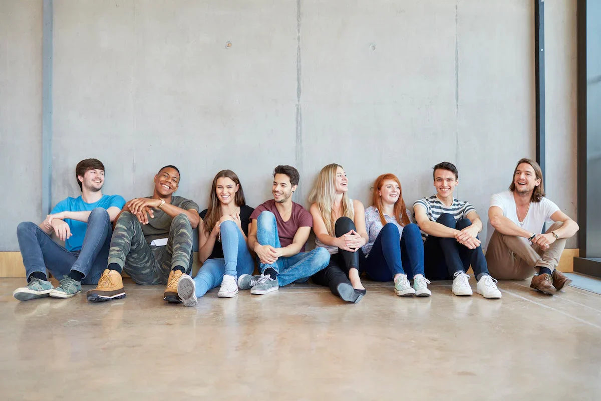Group of people sitting on the floor against a concrete wall.