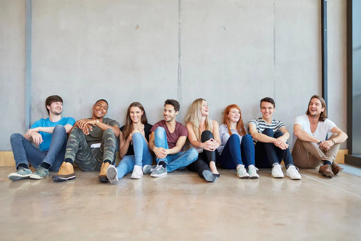 Group of people sitting on the floor against a concrete wall.