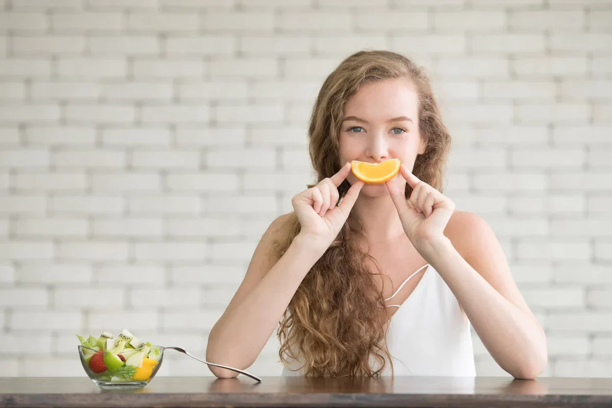 Woman holding an orange slice in front of her face with a blurred background