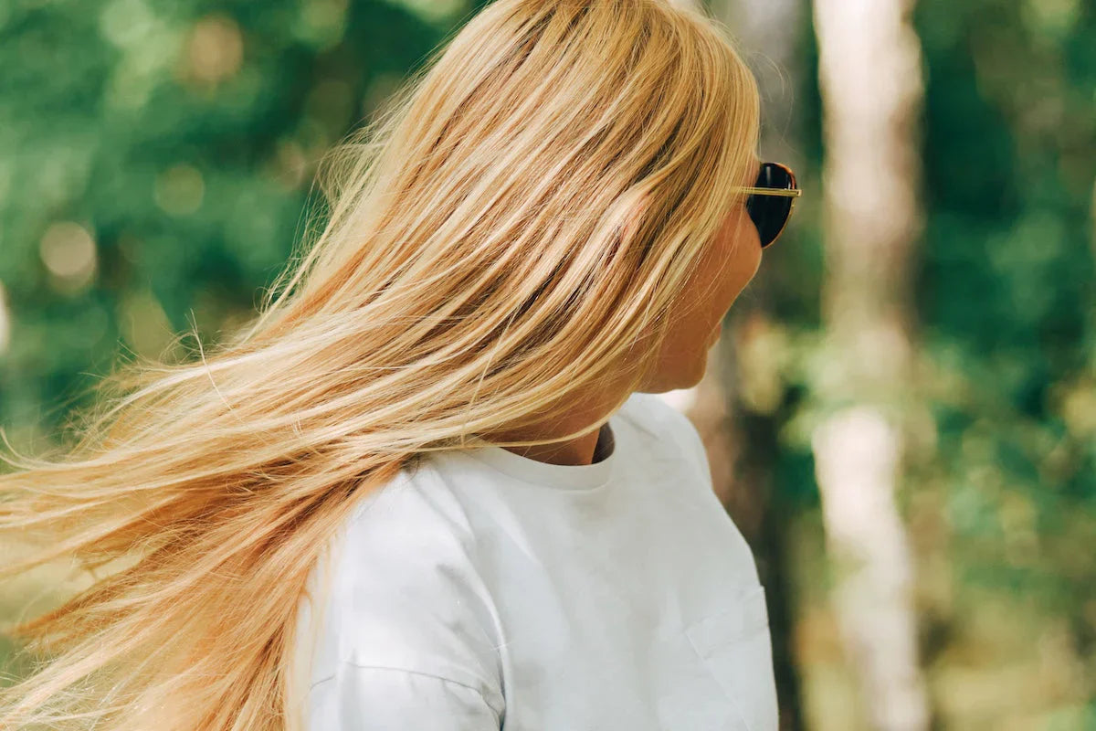Woman with long blonde hair wearing sunglasses in a forest setting