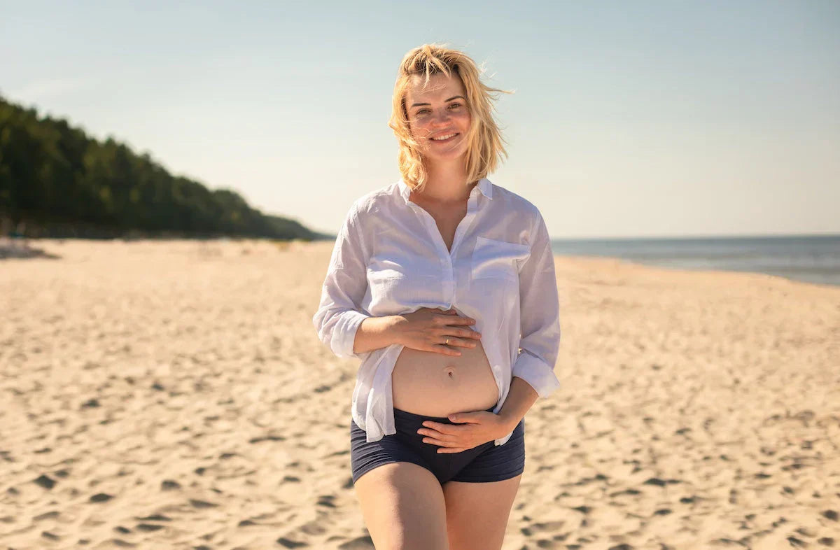 Woman standing on a sandy beach wearing a white shirt and dark shorts.
