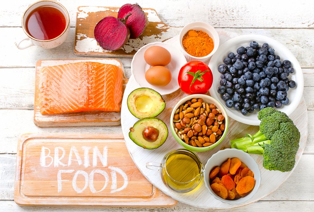A flat lay of various "Brain Food" ingredients artfully arranged on a white wooden surface and cutting boards. 