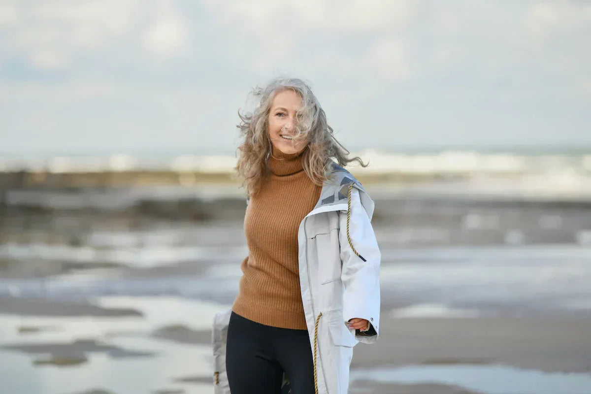 Woman standing on a beach wearing a brown sweater and white coat