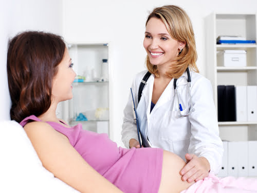 A smiling female doctor examining a pregnant patient during a prenatal check-up.