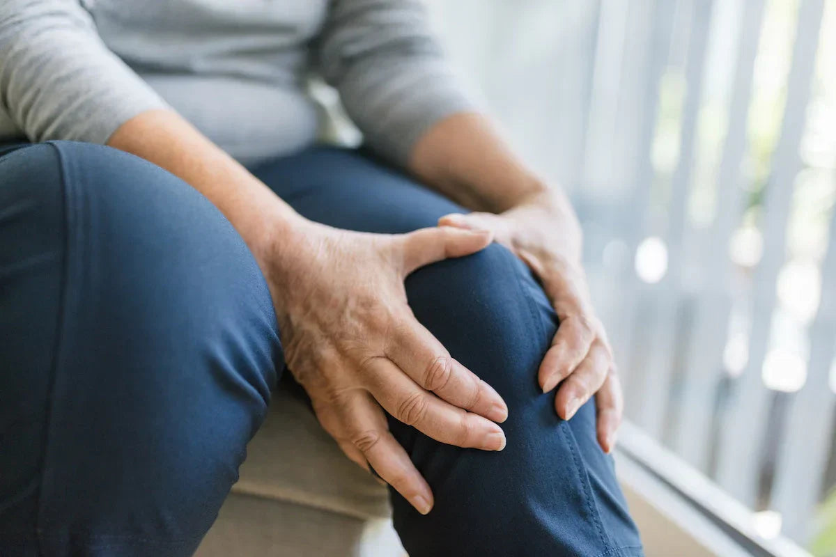 Person holding their knee, possibly indicating pain or discomfort, with a blurred background.