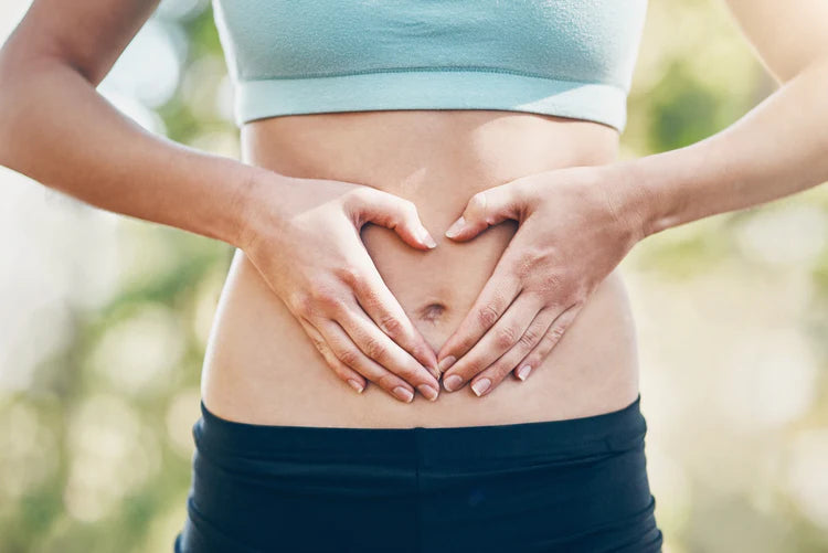 Young woman in sportswear making a heart shape with her hands over her stomach, symbolizing gut health and wellness.